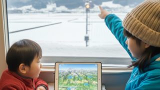 二人の子供が車窓を指さしタブレットを見ている様子
